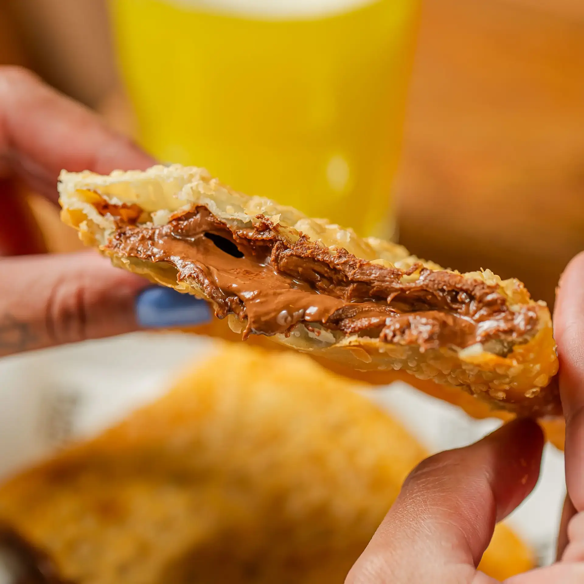 Fotografia mostrando duas mãos segurando o delicioso pastel de nutella com chocolate ao leite do Pastel Mix.